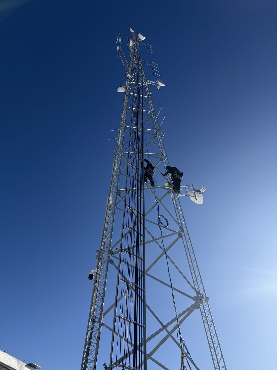Two technicians working on a communications tower equipped with microwave dishes